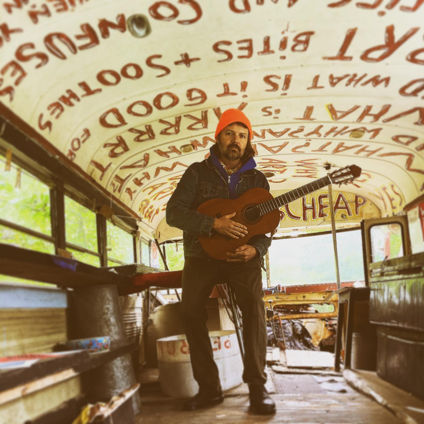 Danny & The Parts poses with guitar in an old gutted bus.