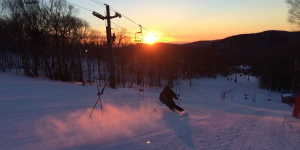 Scenic view of a skiier slaloming on the slopes overlooking a mountain sunset.