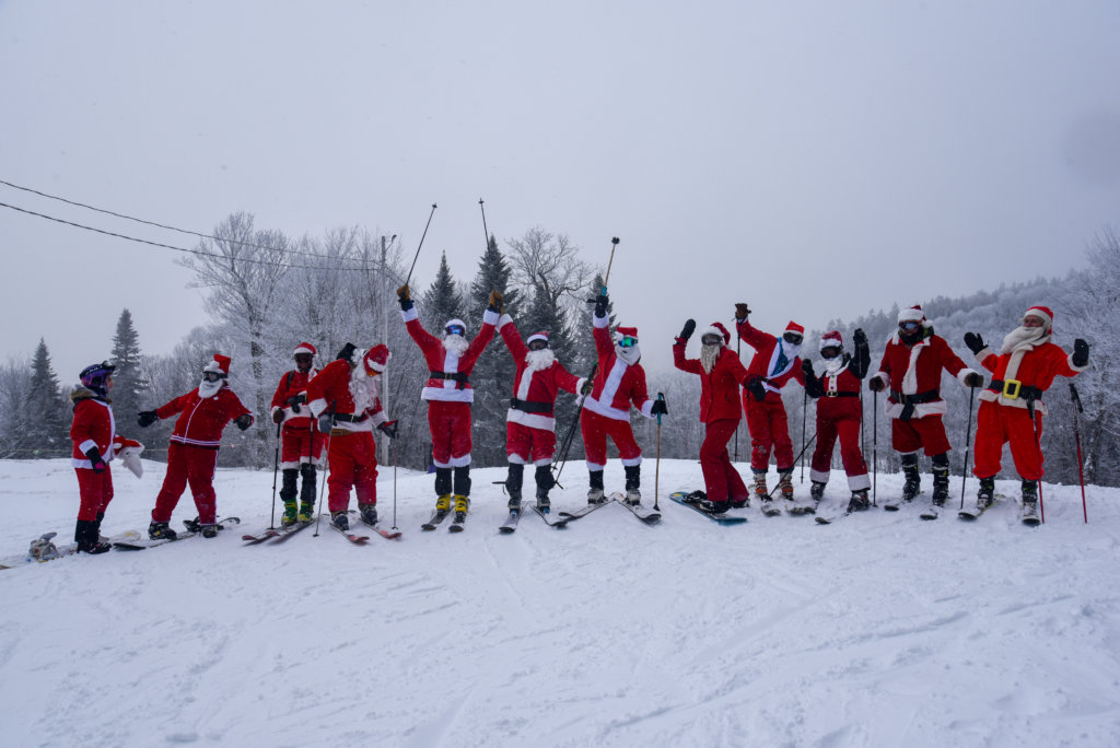 Group shot of Skiers and Snowboarders decked out in Santa Costumes on the base of the mountain.