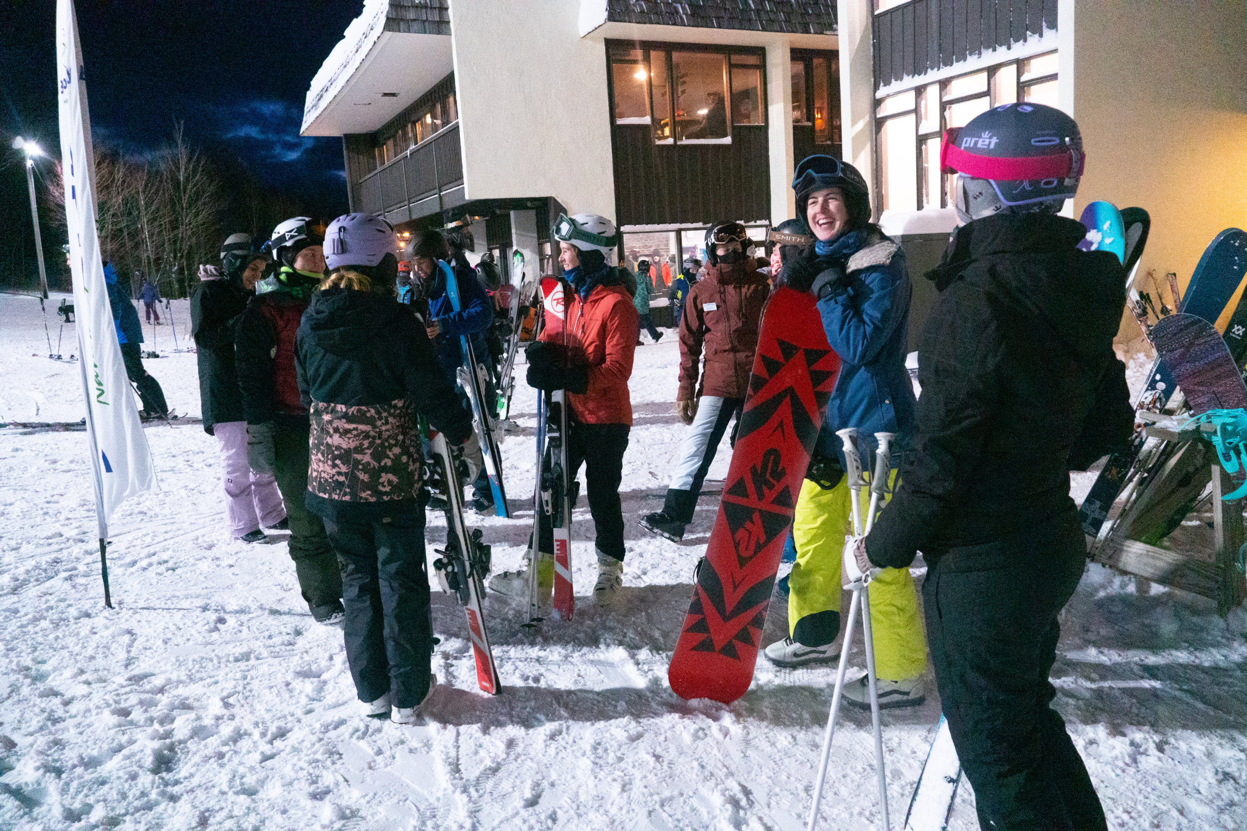 Group of women skiiers and snowboarders with their gear on snow chatting and laughing.
