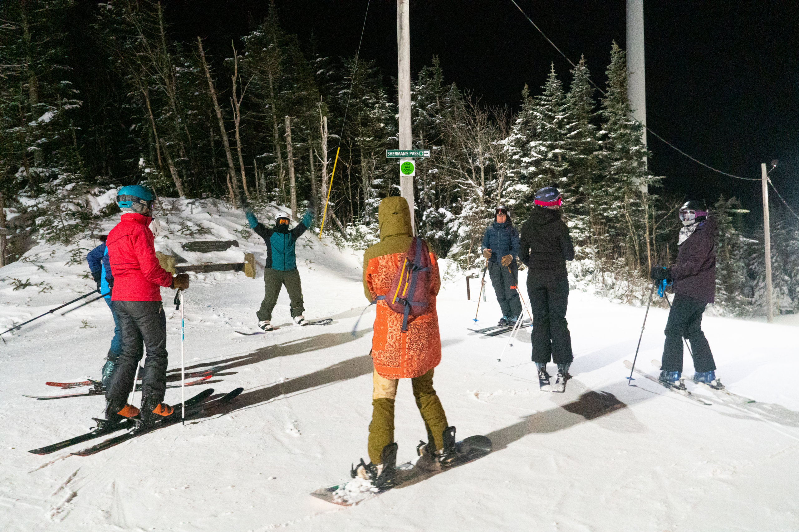 A group of skiiers and riders gathered on the top of the mountain against a night sky
