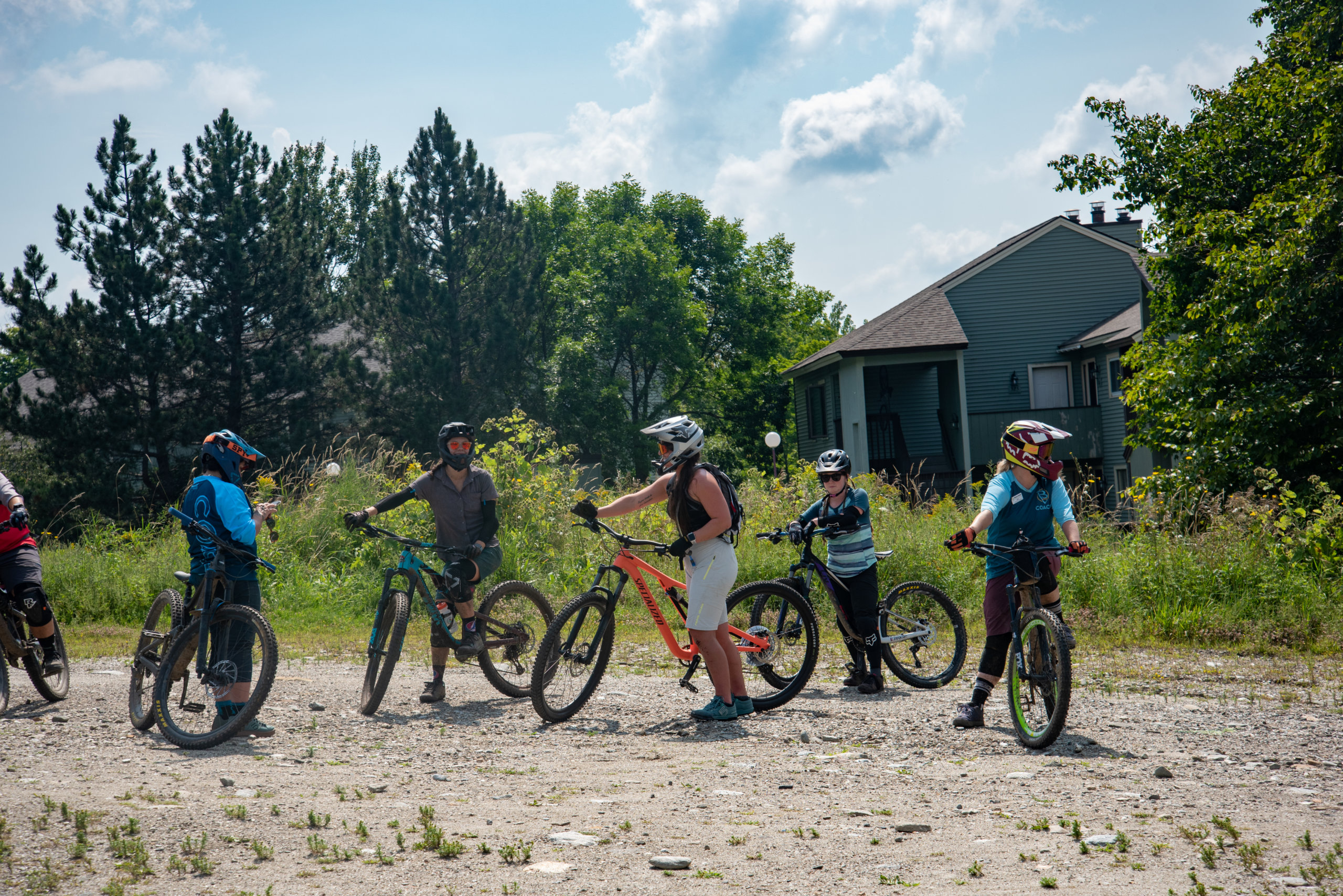 Group of women with their mountain bikes and helmet in tow pause in front of green trees