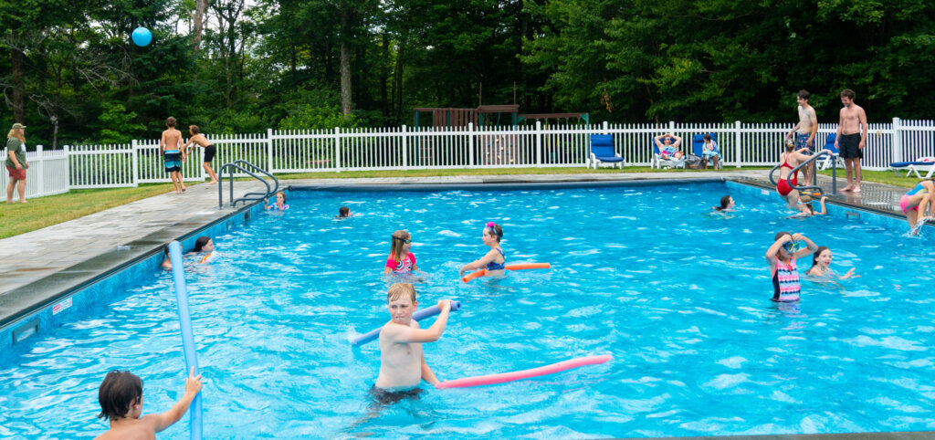 Kids play and splash in outdoor pool against mountainous backdrop.