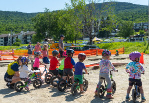 Small children lined up to race on strider bikes with a mountain back drop