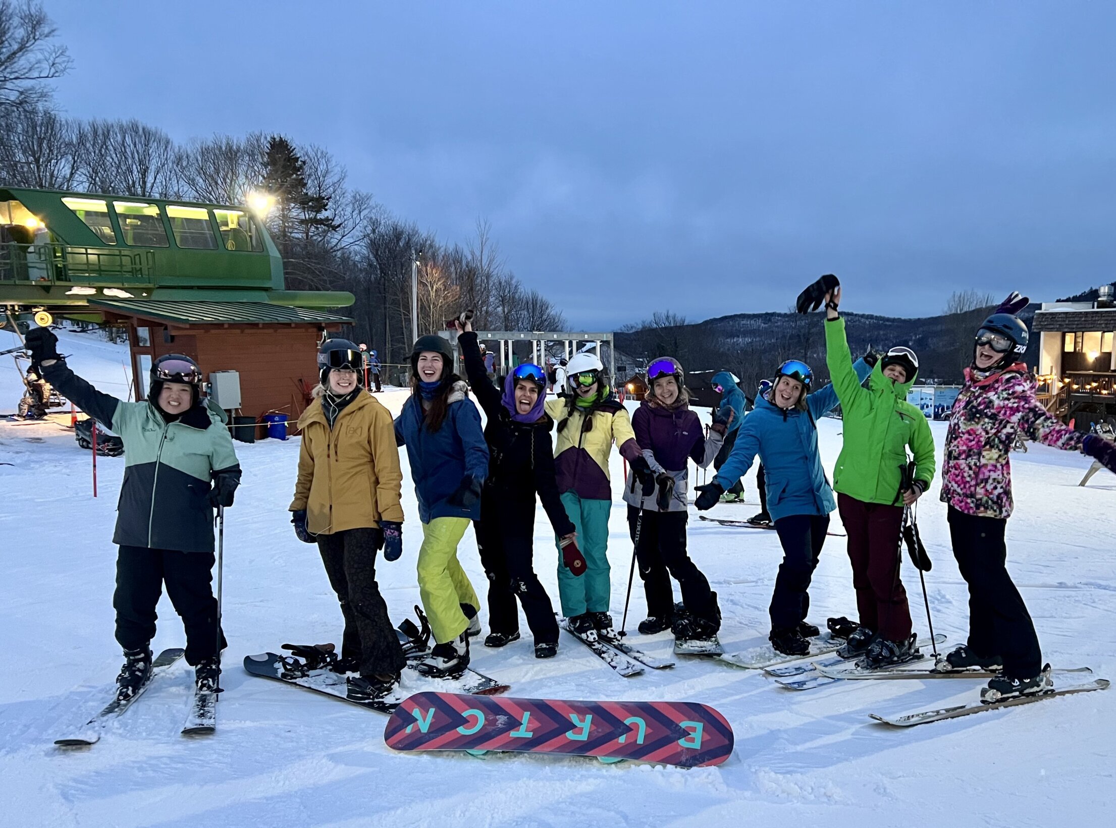 Group of skiiers and snowboarders pose together on the base of the mountain