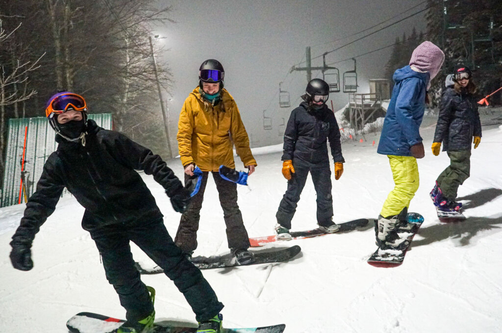 Group of snowboarders gathered at the top of the slopes at night