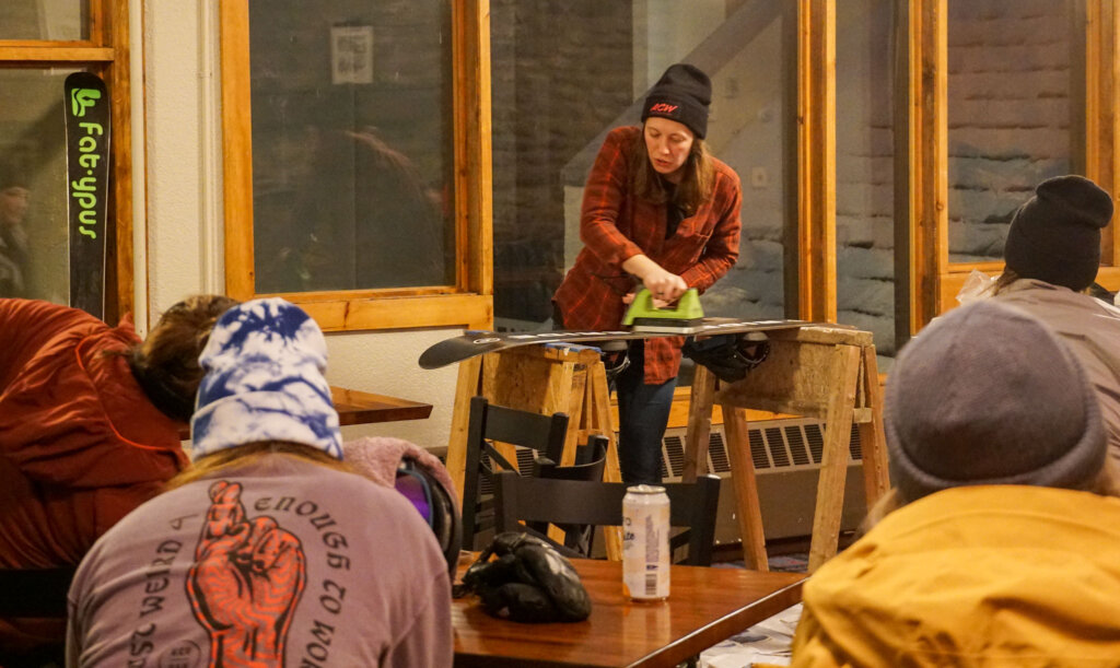 Woman is ironing skis with hot wax as a demonstration to a group of skiers and riders
