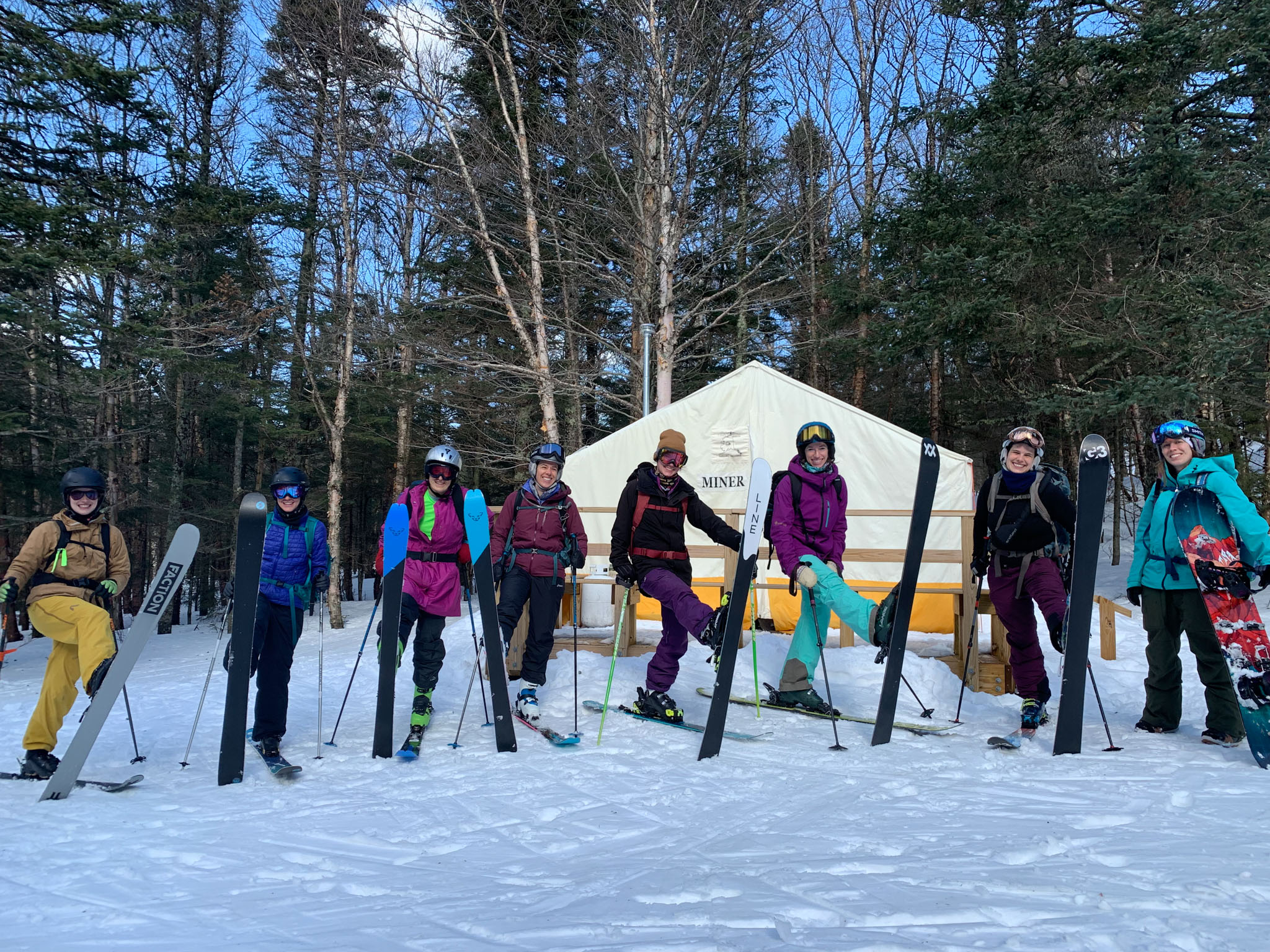 Group of women backcountry skiers and riders pose with one ski in the air