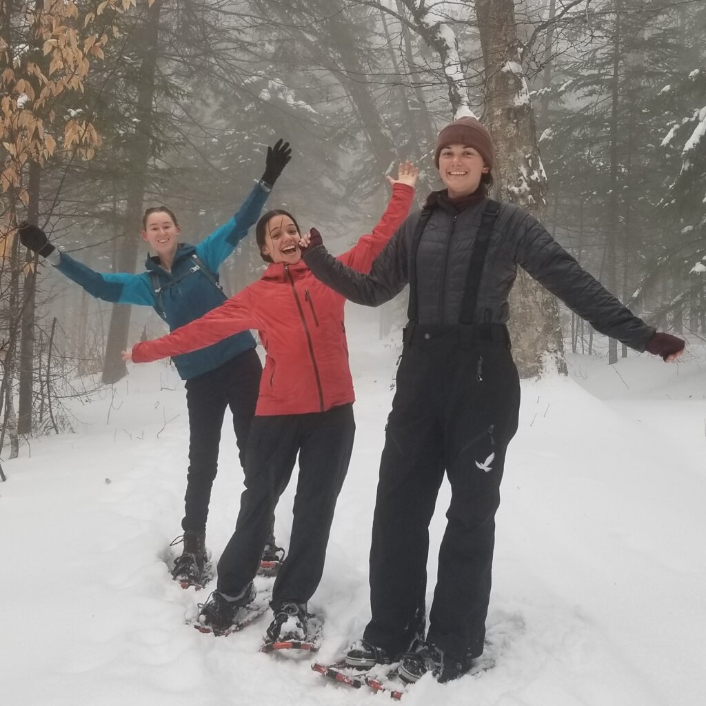 Three women pose on their snowshoes in the backcountry