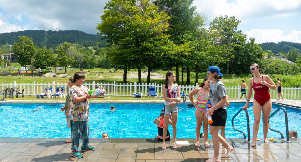 Kids play with water guns in front of outdoor pool overlooking the green mountains