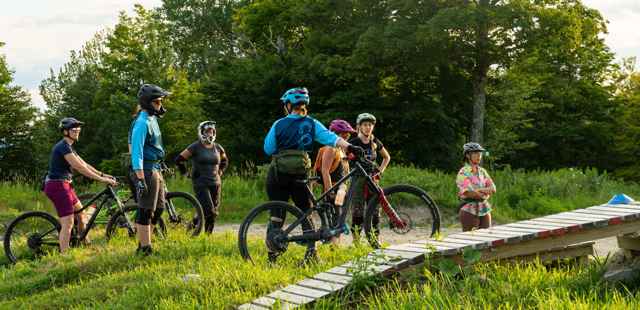 Group of mountain bikers prepare to watch a demonstration over a jump at Bolton Valley