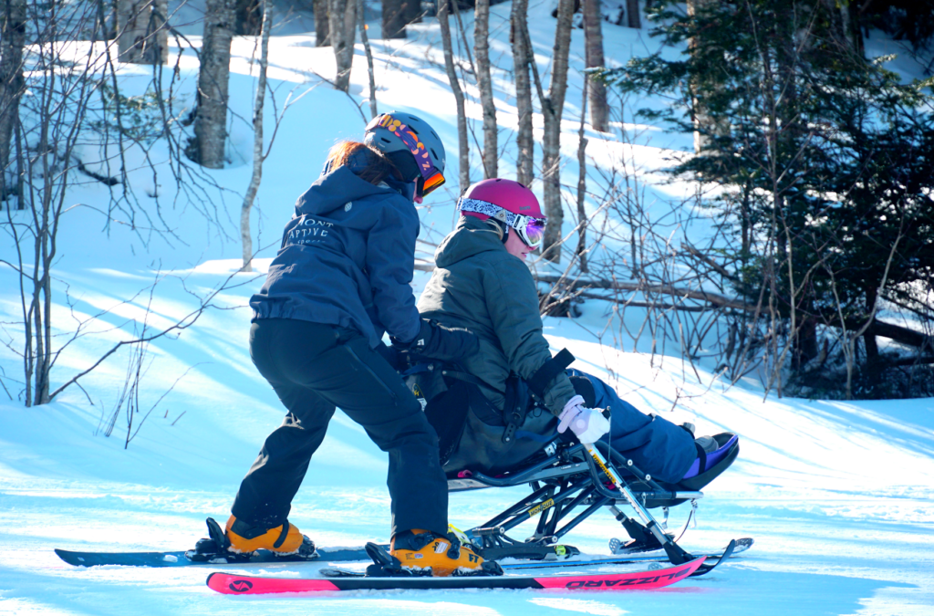 Vermont Adaptive volunteer give adaptive skiier a small push down the slopes