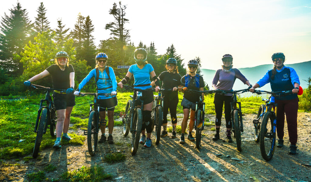 Group of mountain biking women line up on the vista peak with a sunny mountain background