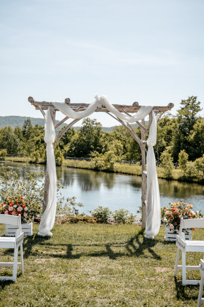 The Ponds exterior with an arbor decorated with a white sheath and white chairs in the background