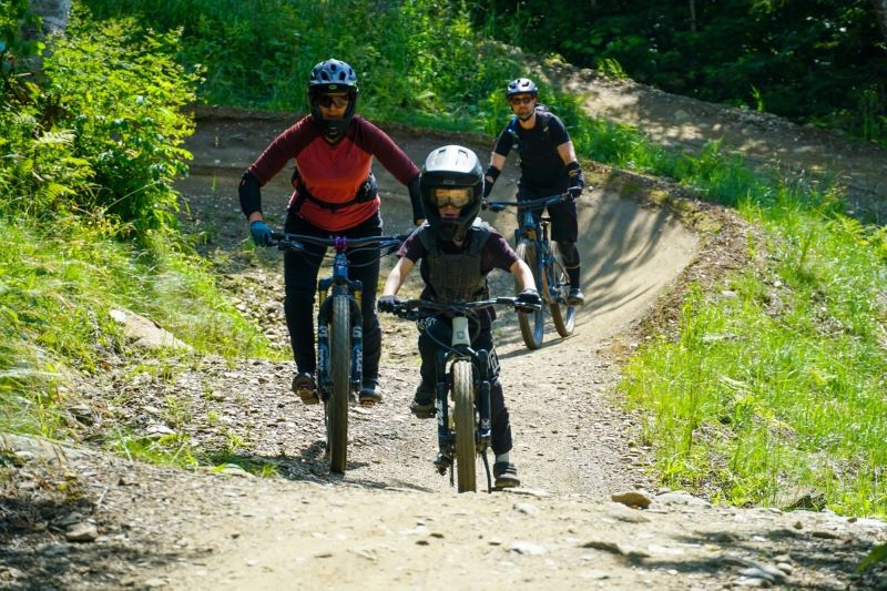 family of mountain bike riders come down a trail surrounded by greenery